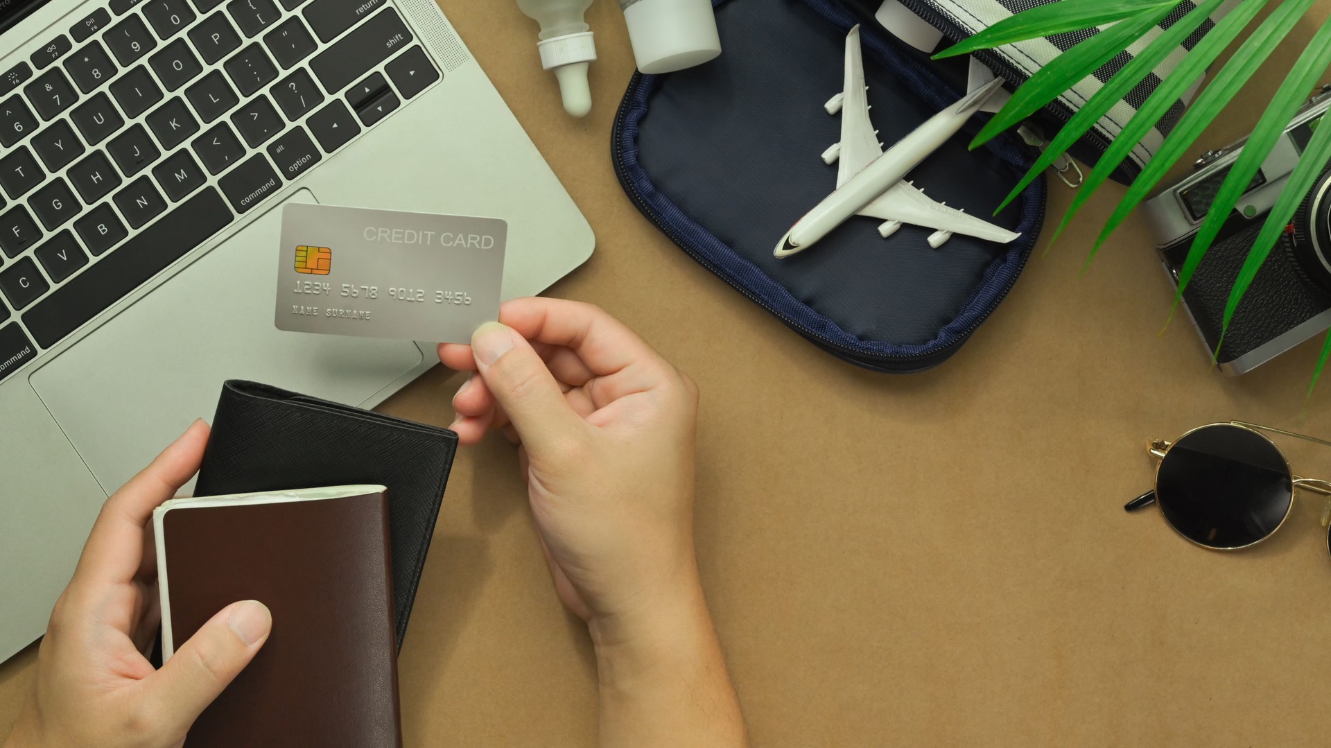 Top view of woman hand holding credit card with travel accessories and passport on desk. Traveling concepts